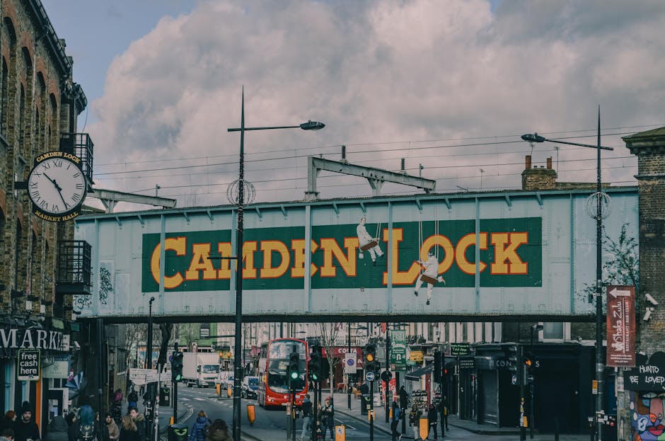 A view of a canal-side building with a brick facade and multiple arched windows on the ground floor, located in an urban area near Camden Town. The building features a large outdoor terrace with table